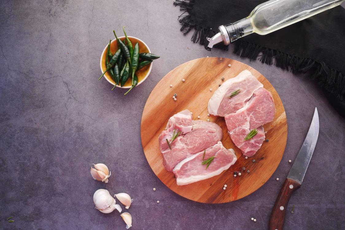 Raw pork slices on a cutting board with garlic and green chillies
